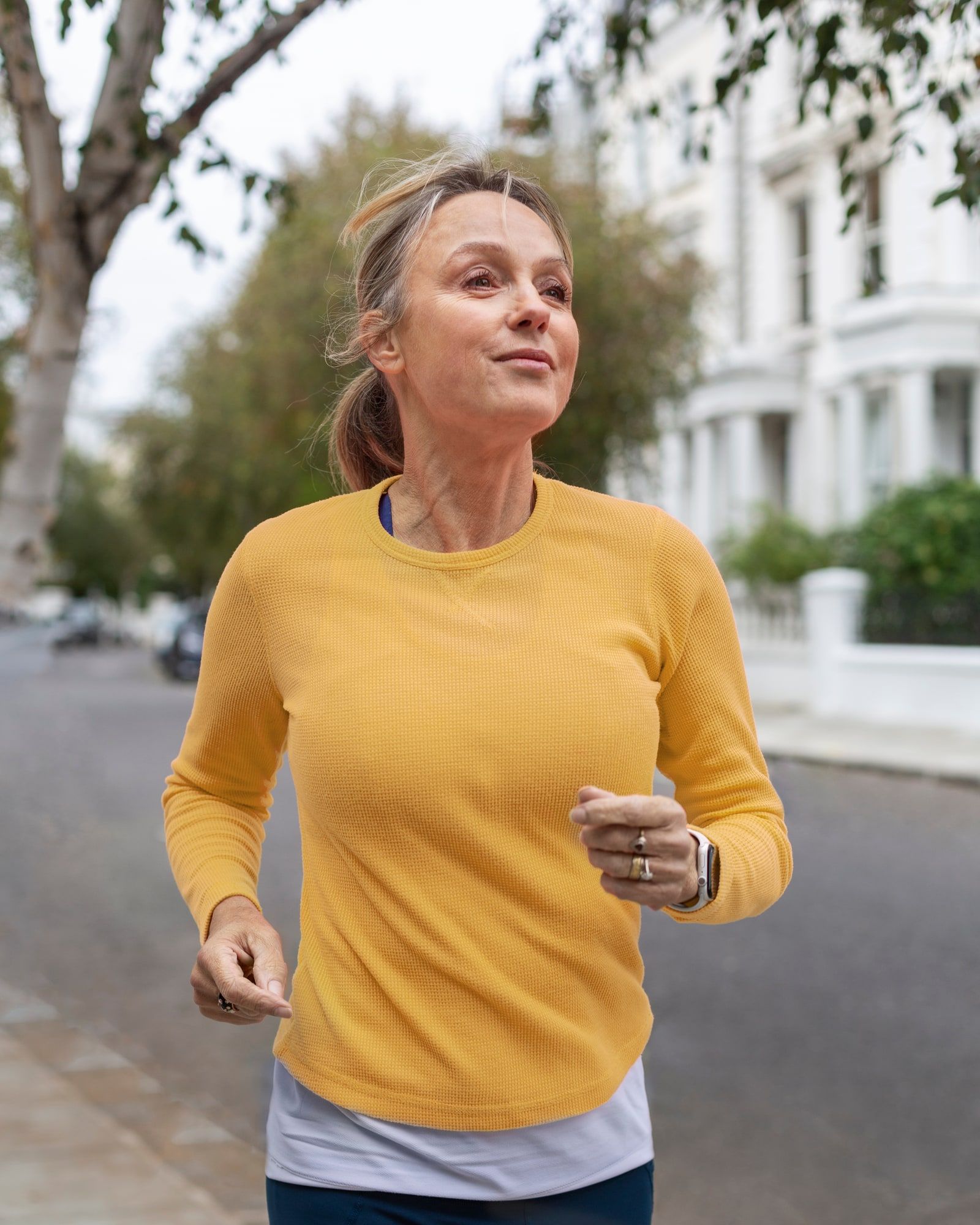 A woman in a yellow top jogging along a quiet residential street, smiling